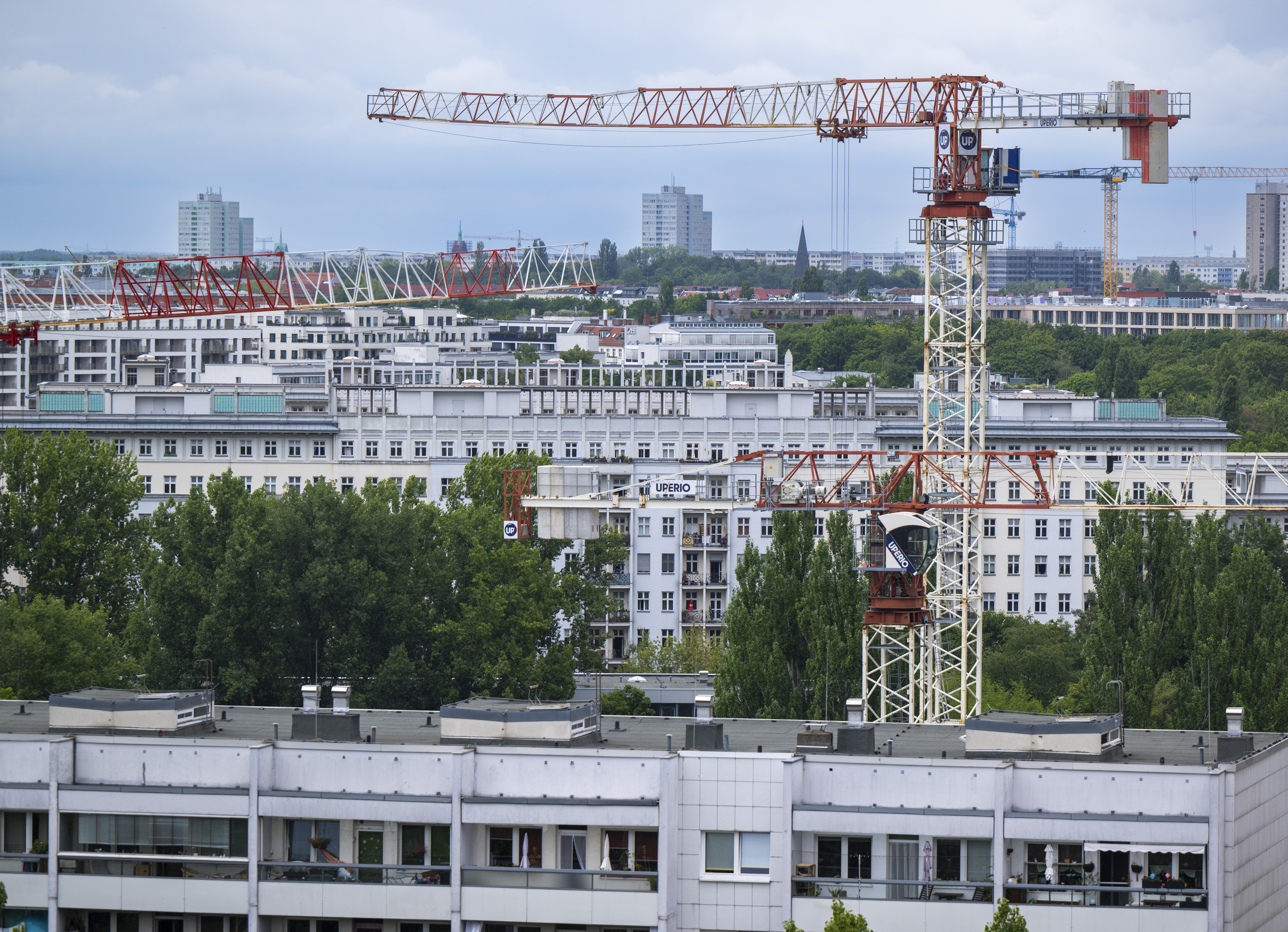 Baukräne ragen in den Himmel vor der Kulisse der Wohnhäuser im Berliner Osten. 