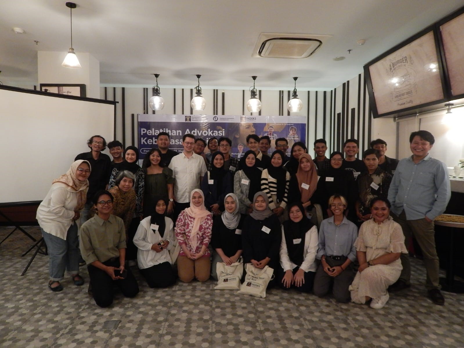 Participants of the event standing alongside Dr. Stefan Diederich, Project Director of FNF Indonesia, in front of a banner showing the event's details.