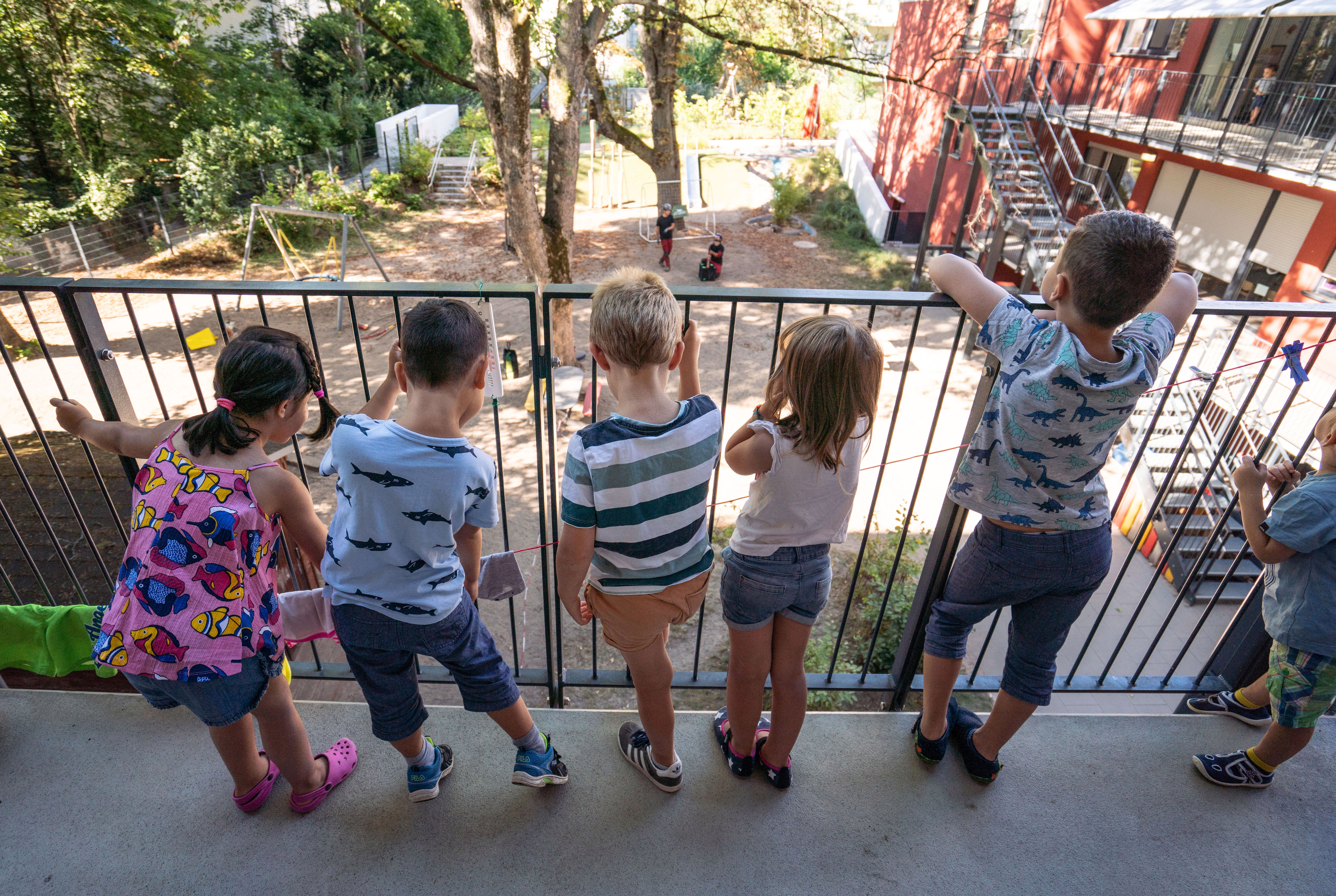 KInder stehen am Geländer und schauen in den Garten einer Kindertagesstätte 