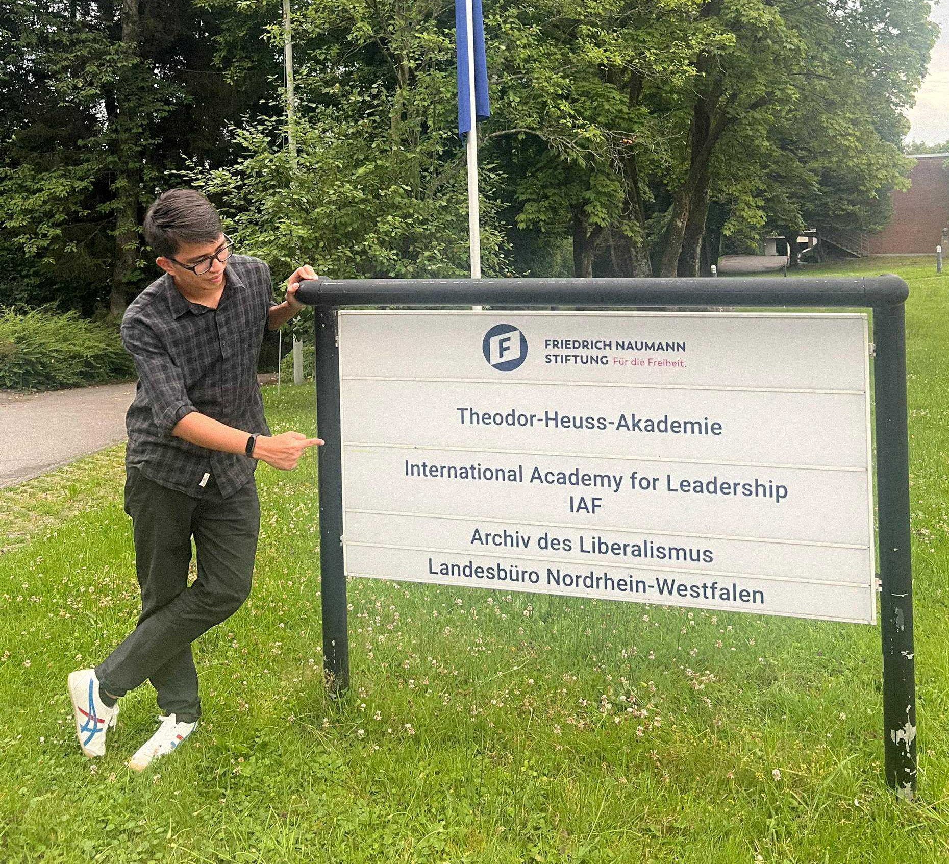 Rahman Imuda standing next to a signboard of IAF in Gummersbach.