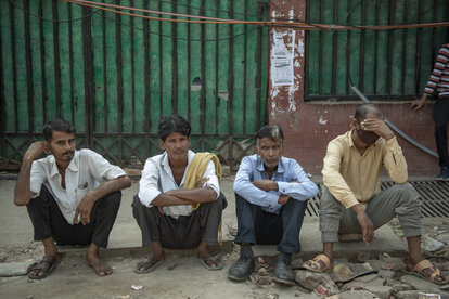 Eine Gruppe von Tagelöhnern sitzt auf einem Bürgersteig, während sie am Labour Chowk in Noida auf Arbeit warten