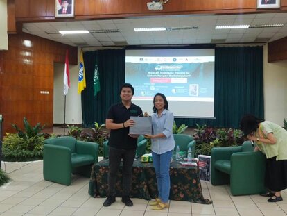 FNF Indonesia's program Officer, Putu Nuansa, is seen standing next to Adwin Pratama Anas (one of the speakers from Eratani). Nuansa is giving Adwin a memento from the event.