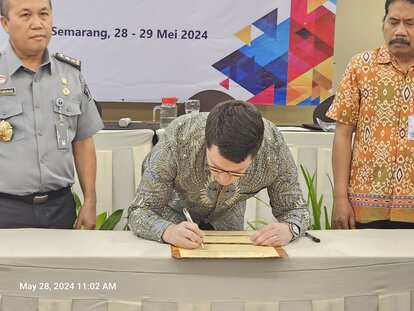 Dr. Stefan Diederich signing the Annual Work Plan document with Hantor Situmorang and Agung Kristianto seen standing on either side of him.