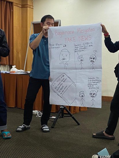 Two participants presenting the result of their brainstorming session. The paper they are holding shows a four panel comic titled, &quot;How to Counter Fake News&quot;