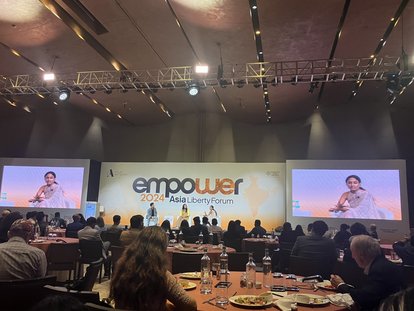 Three speakers were seen sitting on their respective seats on a stage. The banner of Asia Liberty Forum 2024 spanned behind them.