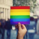 LGBT community member holding a protest banner with pride flag 