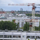 Baukräne ragen in den Himmel vor der Kulisse der Wohnhäuser im Berliner Osten. 