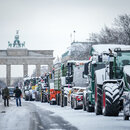 Zahlreiche schneebedeckte Traktoren stehen auf der Straße des 17. Juni vor dem Brandenburger Tor.