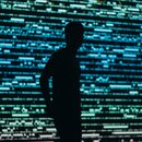 Dark silhouette of a person in front of a big screen full of gree and blue data