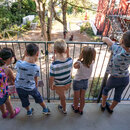 KInder stehen am Geländer und schauen in den Garten einer Kindertagesstätte 